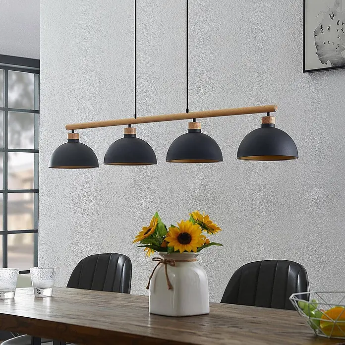 Lindby Pendelleuchte Tirzana - schwarz, Schwarz, gold, holz hell, E27 - Vierflammige Pendelleuchte mit schwarzen Kuppelschirmen und Holzleiste über einem Esstisch.