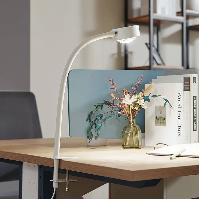 Lindby Klemmleuchte Jyla - Farbe Gehäuse: weiß / opal - Weiße Klemm-Schreibtischlampe mit flexiblem Schwanenhals und LED-Kopf, die einen Holzschreibtisch beleuchtet.