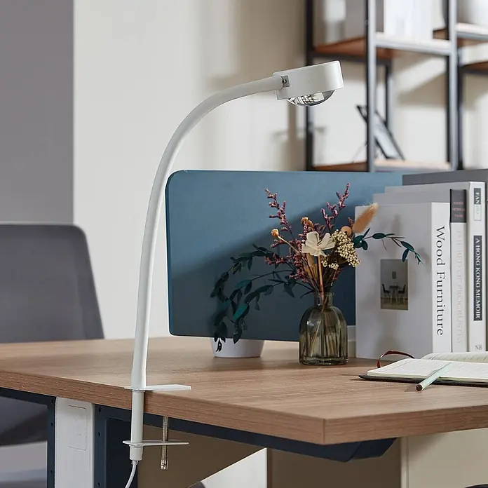 Lindby Klemmleuchte Jyla - Farbe Gehäuse: weiß / opal - Weiße, flexible LED-Schreibtischlampe an einem Holzschreibtisch befestigt, beleuchtet einen Arbeitsplatz.
