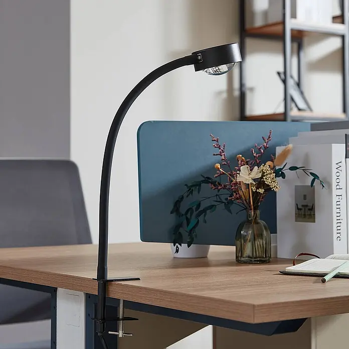 Lindby Klemmleuchte Jyla - Farbe Gehäuse: schwarz - Eine schwarze, flexible Schreibtischlampe mit rundem Kopf, an einem hellen Holzschreibtisch befestigt, beleuchtet den Arbeitsplatz.
