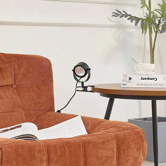 Lindby Klemmleuchte Jyla - Farbe Gehäuse: schwarz - Schwarze Klemmspotleuchte an Holztischplatte befestigt, ideal zum Lesen im orangefarbenen Kordsessel.