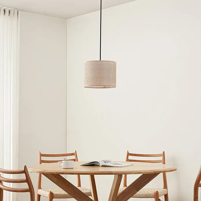 Lindby Pendelleuchte Soula - creme / amber, beige, E27 - Eine hellbeige Pendelleuchte aus Geflecht hängt über einem Holzesstisch.