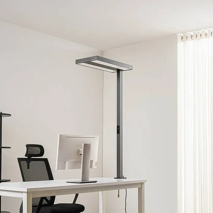 Arcchio Klemmleuchte Logan - Farbe Gehäuse: schwarz - Dunkelgraue LED-Schreibtischlampe auf einem weißen Bürotisch, neben Monitor und Stuhl platziert.