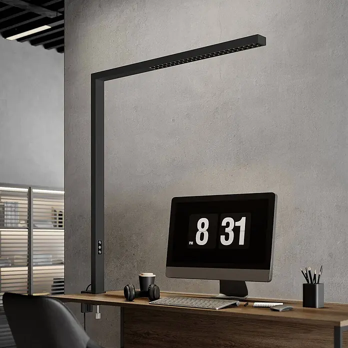 Arcchio Klemmleuchte Jolinda - Farbe Gehäuse: schwarz - Schwarze L-förmige LED-Schreibtischlampe an einem Holztisch, die einen modernen Büroarbeitsplatz mit Computer beleuchtet.
