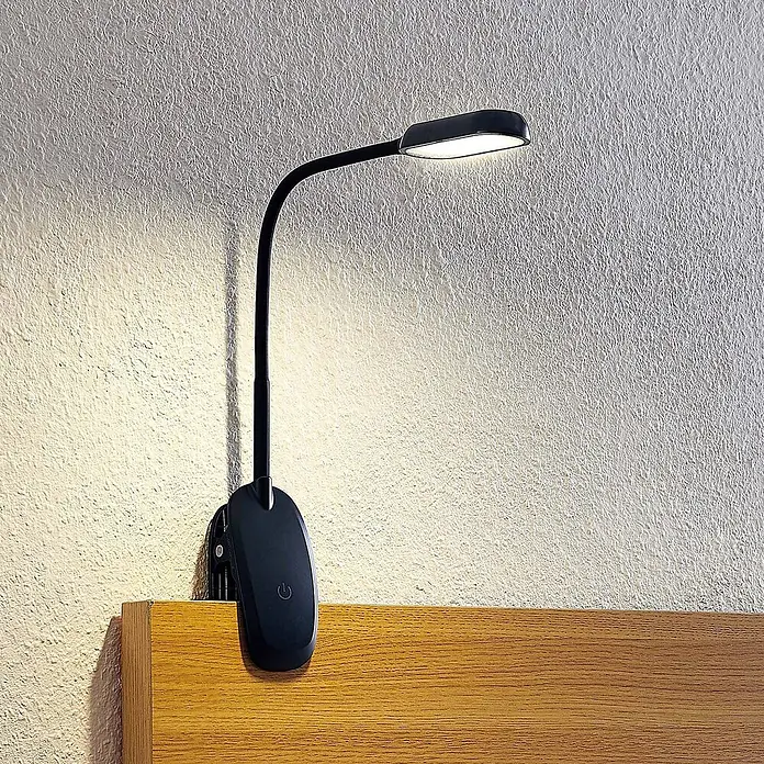 Prios Klemmleuchte Najari - Farbe Gehäuse: schwarz - Schwarze LED-Klemmleuchte mit flexiblem Hals an einem Holzkopfteil befestigt, beleuchtet eine strukturierte Wand.