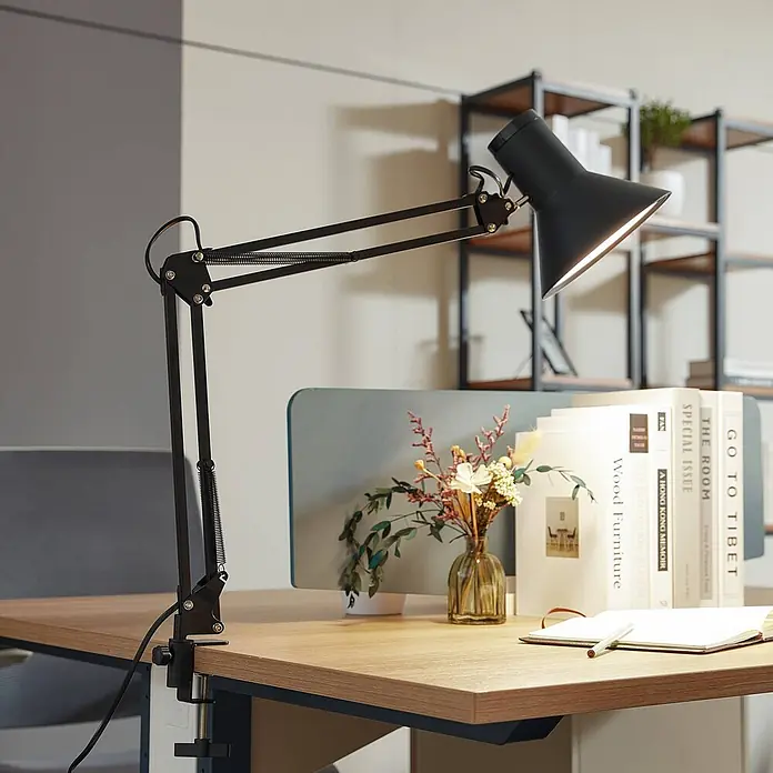 Lindby Klemmleuchte Undra - Farbe Gehäuse: schwarz - Schwarze, verstellbare Schreibtischlampe mit Metallarm, an einem Holzschreibtisch befestigt, beleuchtet den Arbeitsbereich.