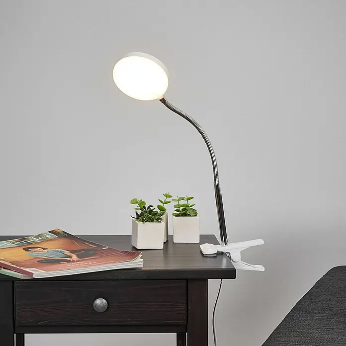 Lindby Klemmleuchte Milow - L x B x H: 11,3 x 10 x 36 cm, Farbe Gehäuse: weiß / opal - Weiße LED-Klemmleuchte mit flexiblem Chrom-Schwanenhals, an einem dunklen Holztisch befestigt.