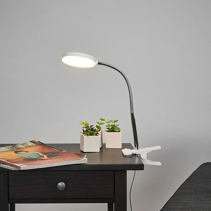 Lindby Klemmleuchte Milow - L x B x H: 11,3 x 10 x 36 cm, Farbe Gehäuse: weiß / opal - Weiße LED-Klemmleuchte mit flexiblem silbernem Schwanenhals, die einen dunklen Nachttisch beleuchtet.