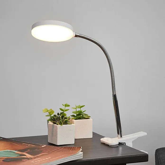 Lindby Klemmleuchte Milow - L x B x H: 11,3 x 10 x 36 cm, Farbe Gehäuse: weiß / opal - Weiße LED-Klemmleuchte mit flexiblem silbernem Schwanenhalsarm, an einem dunklen Schreibtisch befestigt.