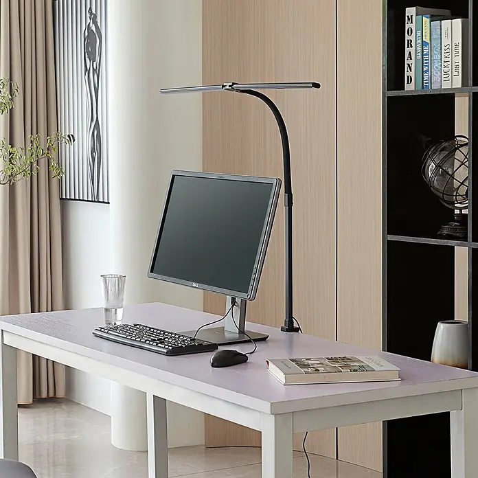 Lindby Klemmleuchte Nilay - L x B x H: 80 x 4 x 97,5 cm, Farbe Gehäuse: schwarz - Schwarze Schreibtischlampe mit silberner LED-Leiste, die einen Computermonitor und eine Tastatur auf einem hellen Schreibtisch beleuchtet.
