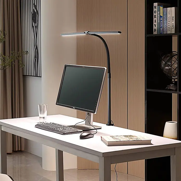Lindby Klemmleuchte Nilay - L x B x H: 80 x 4 x 97,5 cm, Farbe Gehäuse: schwarz - Eine moderne schwarze und silberne LED-Schreibtischlampe beleuchtet einen Computermonitor auf einem hellen Schreibtisch in einem Home-Office.