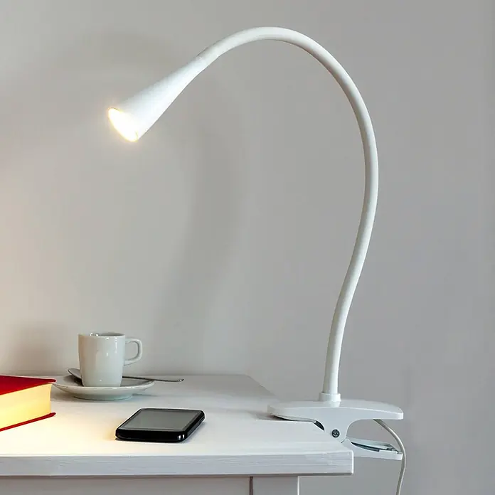Lindby Klemmleuchte Baris - L x B x H: 13 x 6 x 44 cm, Farbe Gehäuse: weiß / opal - Weiße Schreibtischlampe mit flexiblem Schwanenhals und Klemmfuß, beleuchtet einen Schreibtisch mit Buch, Tasse und Handy.