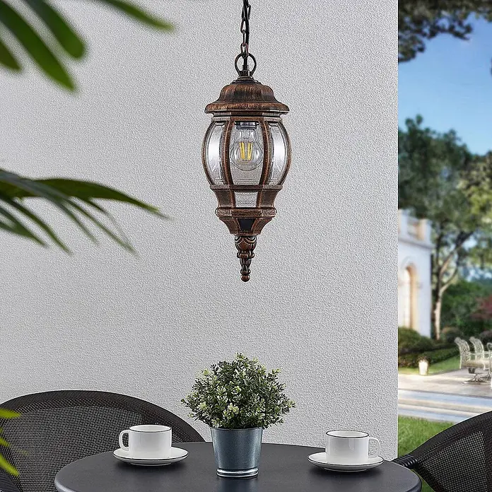 Lindby Außenwand- & Deckenleuchte Nadesha - L x B x H: 16,5 x 16,5 x 38,5 cm, messing / gold, messing / gold, IP44 - Antike Bronze-Hängeleuchte mit Klarglas und LED-Birne, beleuchtet einen Terrassentisch im Freien.