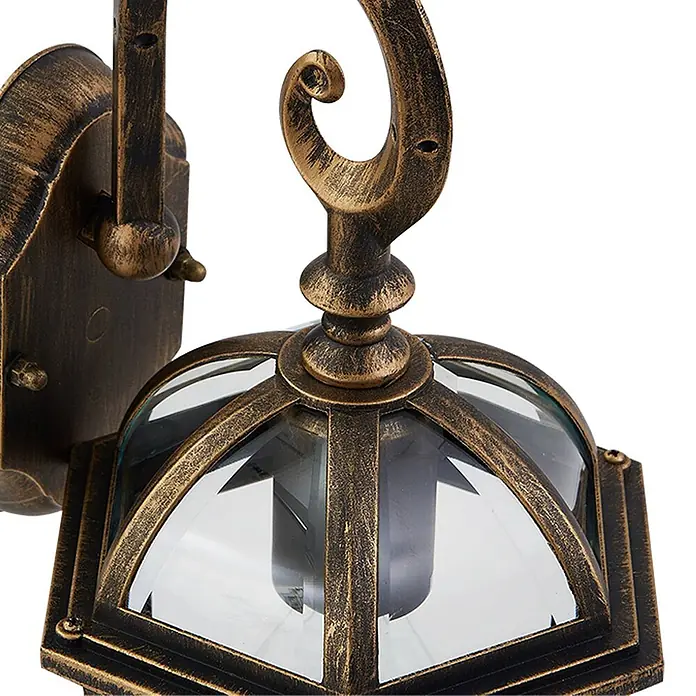Lindby Außenwandleuchte Adelisa - bronze / altmessing, bronze / altmessing, IP44 - Nahaufnahme einer antikgoldenfarbenen Außenwandleuchte mit klaren Glaspaneelen und einem verzierten, geschwungenen Arm.