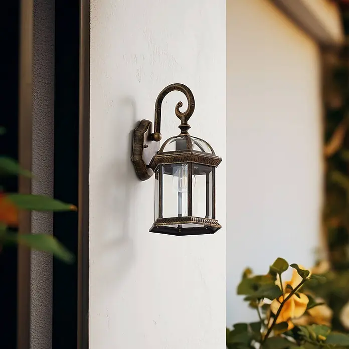 Lindby Außenwandleuchte Adelisa - bronze / altmessing, bronze / altmessing, IP44 - Antik-Messing Außenwandlaterne mit Klarglas an einer Gebäudewand montiert.