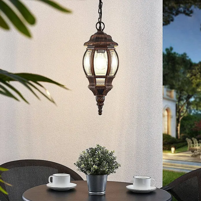 Lindby Außenwand- & Deckenleuchte Nadesha - L x B x H: 16,5 x 16,5 x 38,5 cm, messing / gold, messing / gold, IP44 - Beleuchtete bronzefarbene Outdoor-Hängeleuchte über einem Terrassentisch.