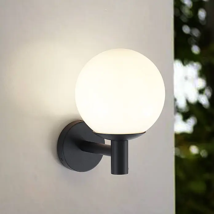 Lindby Außenwandleuchte Dangan - weiß / opal, IP44 - Schwarze Außenwandleuchte mit opalem Glaskugel auf heller Wand.