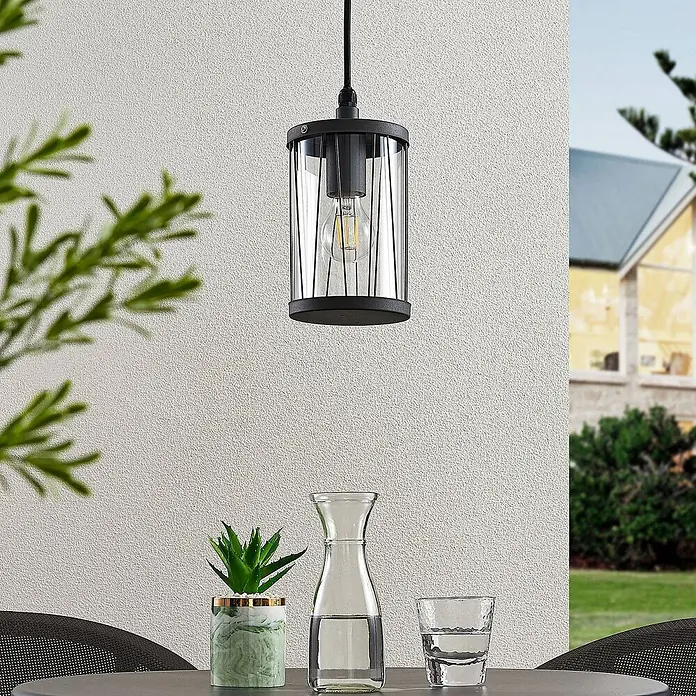 Lindby Außenwand- & Deckenleuchte Yonan - schwarz, schwarz, IP44 - Schwarze Outdoor-Pendelleuchte aus Metall und Glas mit sichtbarer Glühbirne, über einem Terrassentisch hängend.
