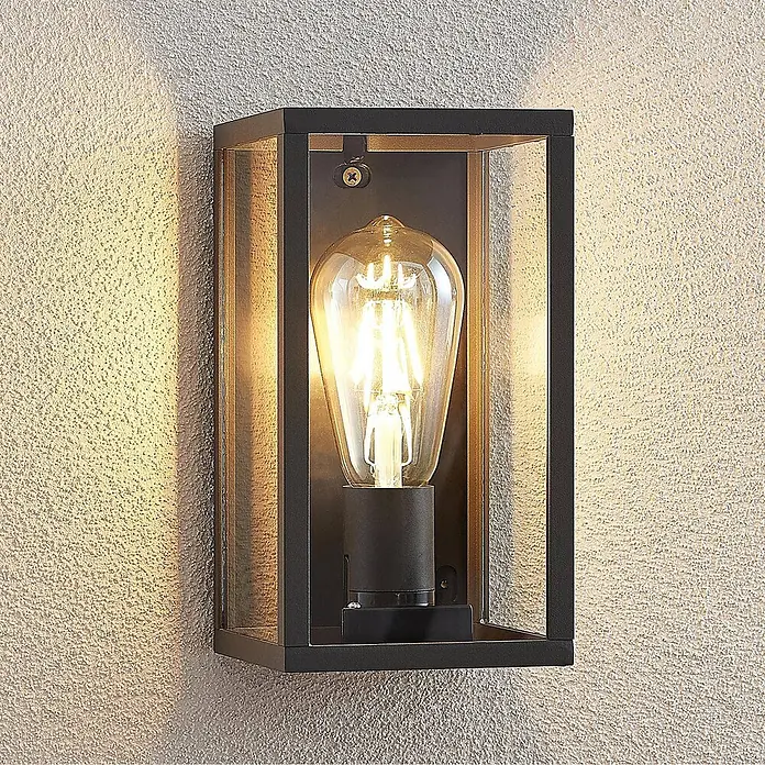 Lindby Außenwandleuchte Filimon - 12 x 12 x 22 cm, schwarz, schwarz, IP44 - Schwarze, rechteckige Wandleuchte mit Klarglas und beleuchteter Vintage-Glühbirne, an einer strukturierten Wand montiert.