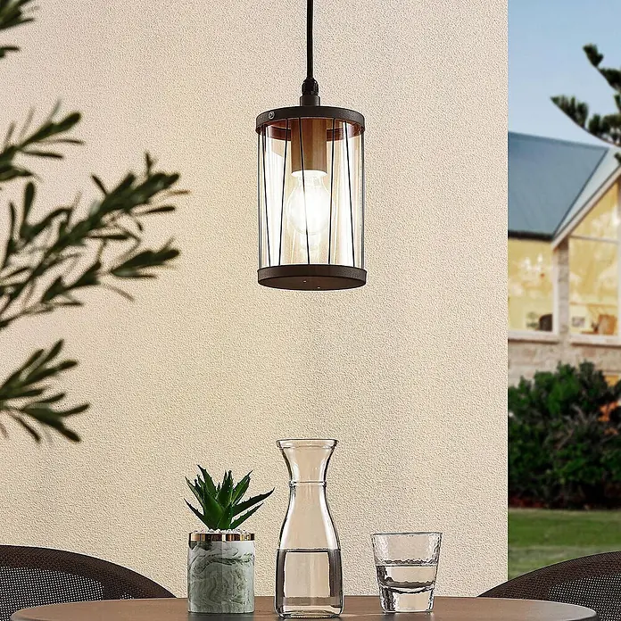 Lindby Außenwand- & Deckenleuchte Yonan - schwarz, schwarz, IP44 - Zylindrische Outdoor-Pendelleuchte mit dunklem Metallrahmen und klarem Glasschirm, die einen Outdoor-Tisch beleuchtet.