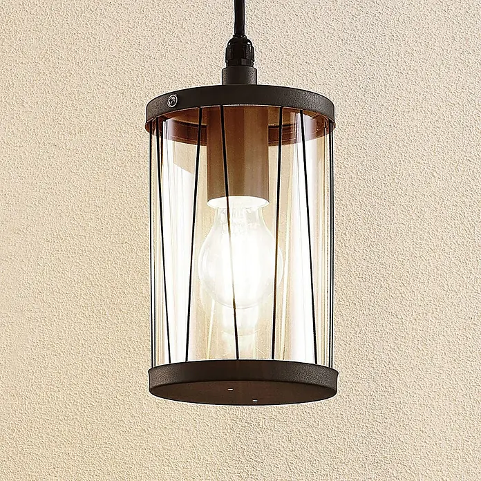 Lindby Außenwand- & Deckenleuchte Yonan - schwarz, schwarz, IP44 - Zylindrische Pendelleuchte mit dunklem Metallrahmen und Klarglasschirm, der eine helle Glühbirne zeigt. Hängt vor einer strukturierten, hellen Wand.