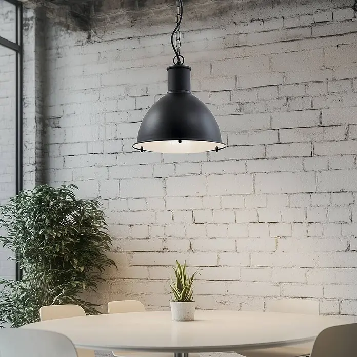 Lindby Außenwand- & Deckenleuchte Luciane - schwarz, IP44 - Schwarze industrielle Pendelleuchte über einem Tisch in einem Raum mit weißer Ziegelwand.