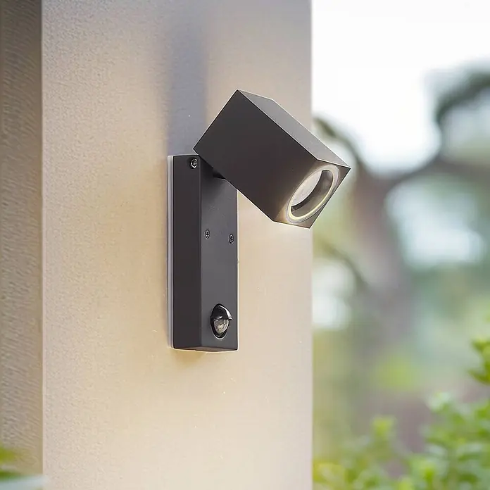 Lindby Außenwandleuchte Othil - alu / grau / zink, alu / grau / zink, IP44 - Schwarze kubische Außenwandleuchte mit Bewegungsmelder an einer Wand.