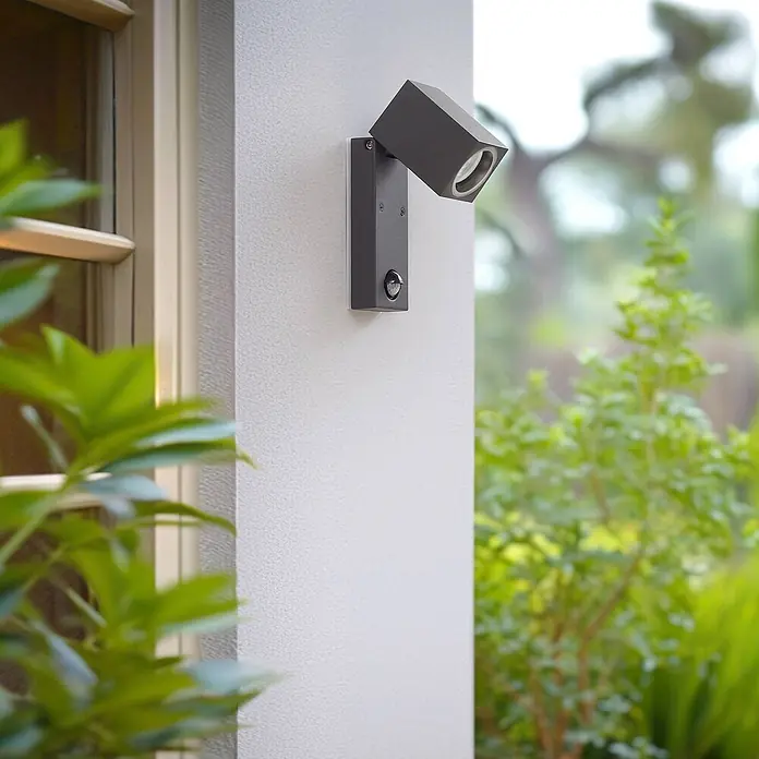 Lindby Außenwandleuchte Othil - alu / grau / zink, alu / grau / zink, IP44 - Dunkelgraue Außenwandleuchte mit schwenkbarem quadratischem Kopf und Bewegungssensor an einer Hauswand.
