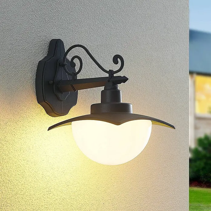 Lindby Außenwandleuchte Elinda - 26,5 x 20 x 28,8 cm, schwarz, schwarz, IP44 - Verzierte schwarze Metall-Außenwandleuchte mit weißem Kugel-Diffusor, an einer strukturierten Wand montiert und warmes Licht spendend.