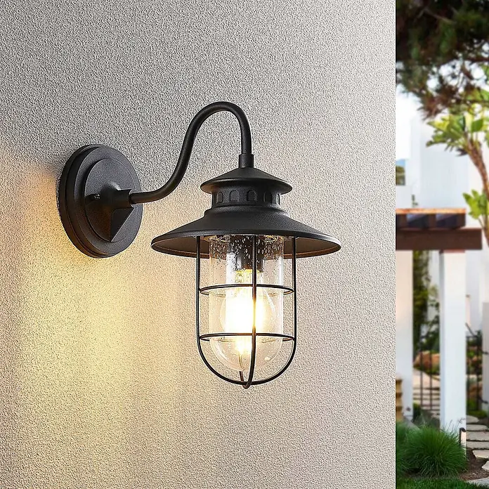 Lindby Außenwandleuchte Kyan - schwarz, IP44 - Schwarze Metall-Außenwandleuchte mit Glas und Käfigdesign, an einer strukturierten Wand montiert. Beleuchtet den Außenbereich.