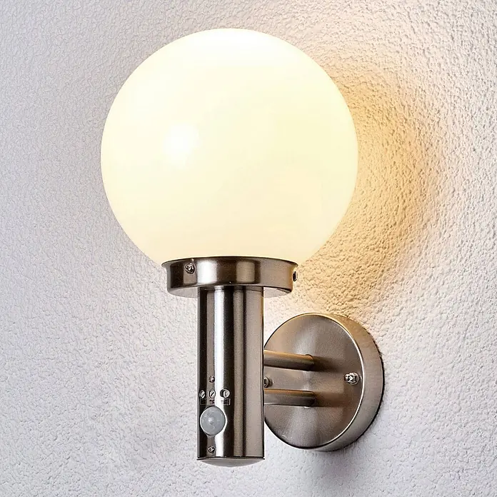 Lindby Außenwandleuchte Nada - 23 x 20 x 33,5 cm, alu / grau / zink, IP44 - Gebürstete Metall-Außenwandleuchte mit kugelförmigem weißem Schirm und integriertem Bewegungssensor, an einer strukturierten Wand montiert.