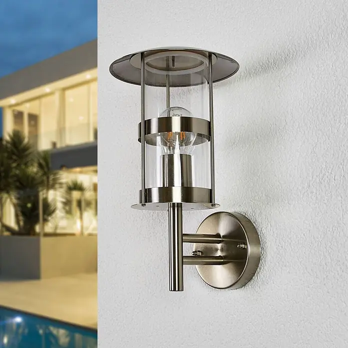 Lindby Außenwandleuchte Noemi - alu / grau / zink, alu / grau / zink, IP44 - Gebürstete Metall- und Glas-Außenwandleuchte mit Edison-Birne, an Hausfassade montiert.
