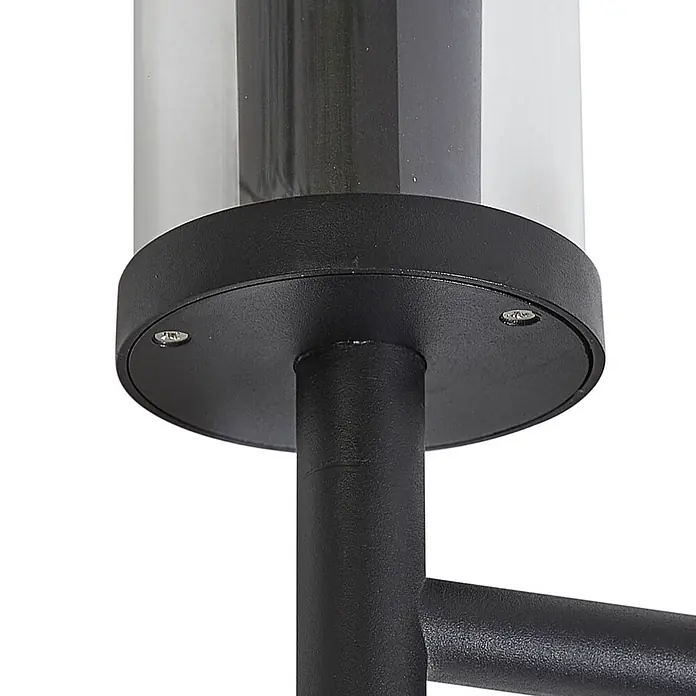 Lucande Außenwandleuchte Zanta - schwarz, klar / transparent, IP54 - Nahaufnahme einer schwarzen, texturierten Außenleuchtenbasis mit einem klaren zylindrischen Diffusor, zeigt die Verbindung zu Stange und Arm.