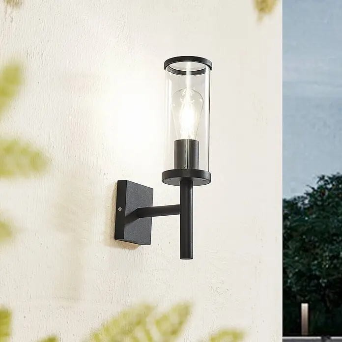 Lucande Außenwandleuchte Zanta - schwarz, klar / transparent, IP54 - Schwarze Außenwandleuchte mit klarem Glaszylinder und sichtbarer Glühbirne an einer strukturierten Wand.