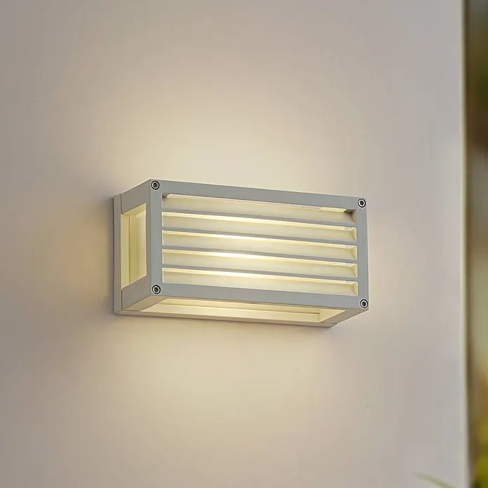 Lucande Außenwandleuchte Aurelien - weiß / opal, IP54 - Rechteckige graue Lamellen-Außenwandleuchte an einer Wand, die warmes Licht abstrahlt.
