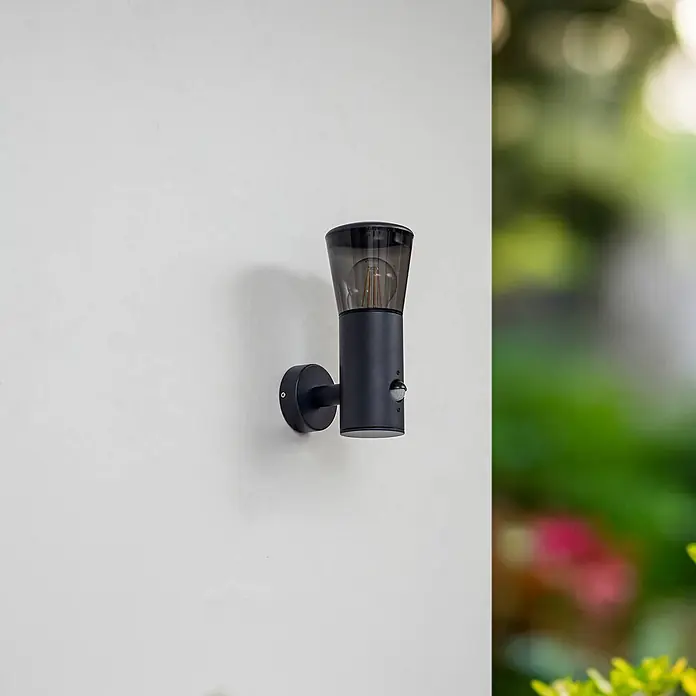 Lindby Außenwandleuchte Heulo - schwarz, schwarz, IP44 - Schwarze Außenwandleuchte mit Bewegungssensor, mit sichtbarer Glühbirne, an einer Wand montiert.