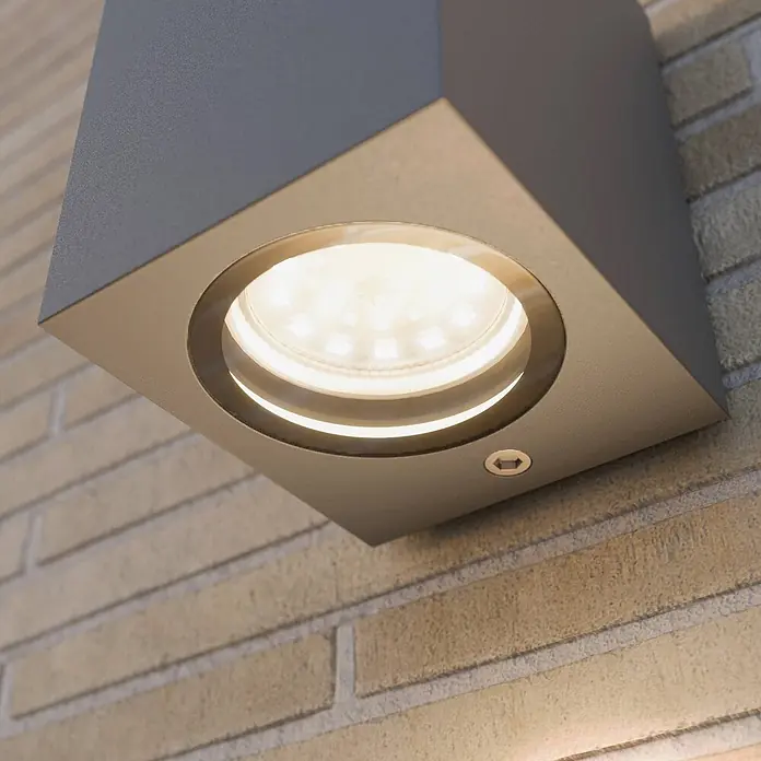 Lucande Außenwandleuchte Xava - schwarz, schwarz, IP65 - Graue quadratische Außenwandleuchte mit beleuchteten LEDs, an einer Ziegelwand montiert.