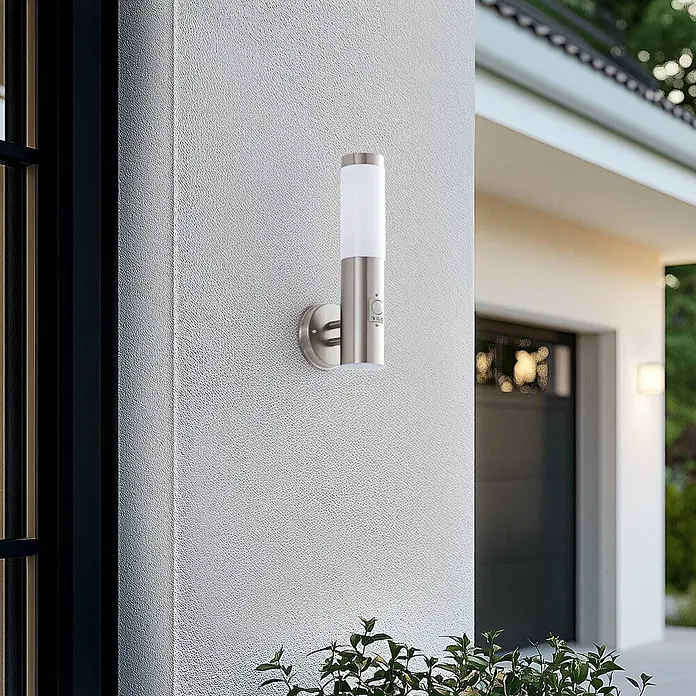 Lindby Außenwandleuchte Kristof - alu / grau / zink, alu / grau / zink, IP44 - Gebürstete Edelstahl-Außenwandleuchte mit weißem Diffusor und integriertem Bewegungsmelder, an einer strukturierten Außenwand montiert.