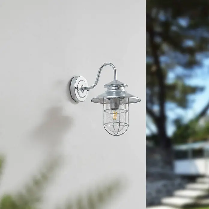 Lindby Außenwandleuchte Naleta - alu / grau / zink, IP44 - Verzinkte silberne Außenwandleuchte mit strukturiertem Glas und Schutzgitter an einer Außenwand.