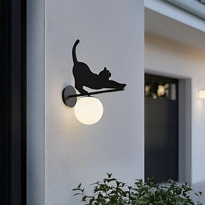 Lindby Außenwandleuchte Katti Cat - 45 x 15 x 40 cm, schwarz, weiß / opal, IP44 - Dekorative schwarze Wandleuchte in Katzenform mit leuchtender weißer Kugel, an einer Außenwand montiert.