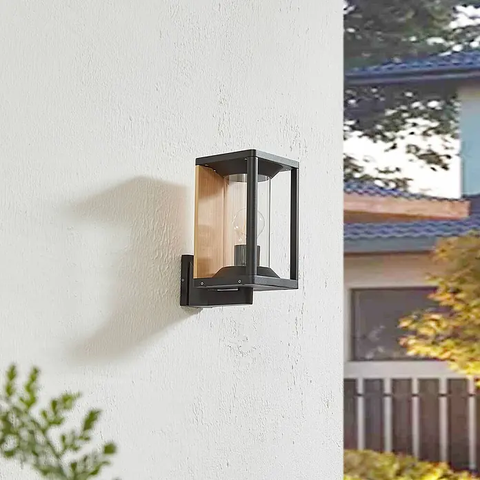 Lucande Außenwandleuchte Candina - 20 x 14,6 x 27,6 cm, schwarz, klar / transparent, IP65 - Außenwandleuchte aus schwarzem Metall, klarem Glas und hellem Holz, an einer Außenwand montiert.