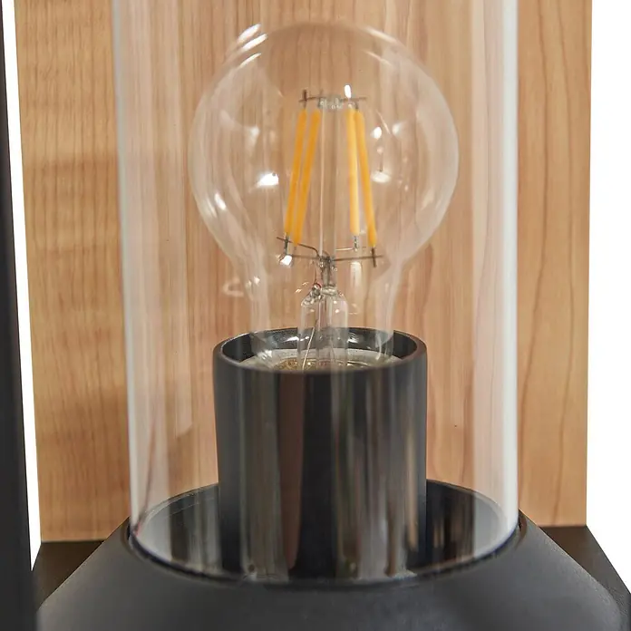 Lucande Außenwandleuchte Candina - 20 x 14,6 x 27,6 cm, schwarz, klar / transparent, IP65 - Nahaufnahme einer modernen Wandleuchte aus schwarzem und klarem Glas mit LED-Filamentlampe vor Holzwand.