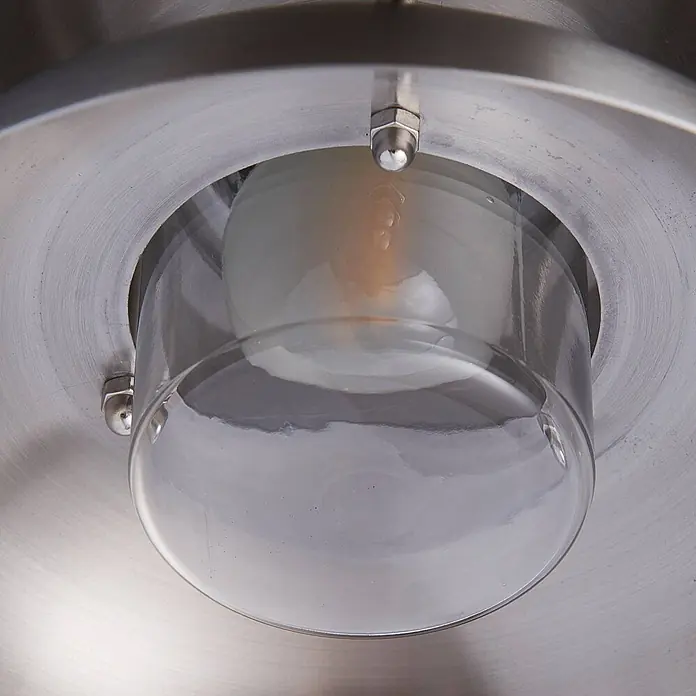 Lucande Außenwandleuchte Thais - alu / grau / zink, IP44 - Nahaufnahme einer Leuchte mit gebürsteter Metallbasis, klarer Glaskuppel und sichtbarer Glühbirne.