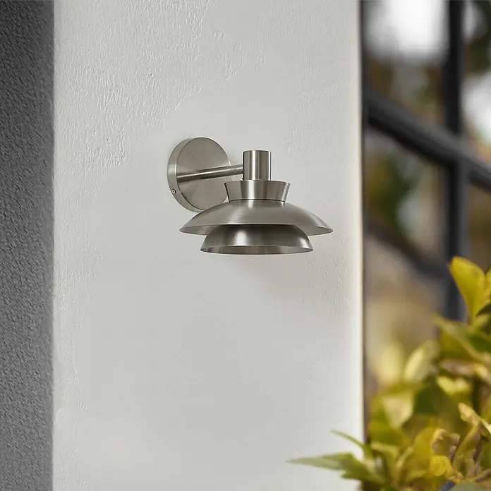 Lucande Außenwandleuchte Thais - alu / grau / zink, IP44 - Gebürstete Nickel-Wandleuchte mit gestuftem, modernem Design, an einer texturierten Wand montiert.