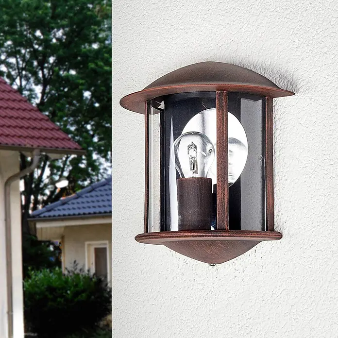 Lindby Außenwandleuchte Maelis - braun / rost, IP44 - Rustikale, rostbraune Außenwandleuchte aus Metall mit klaren Glaspaneelen, an einer weißen Wand montiert.