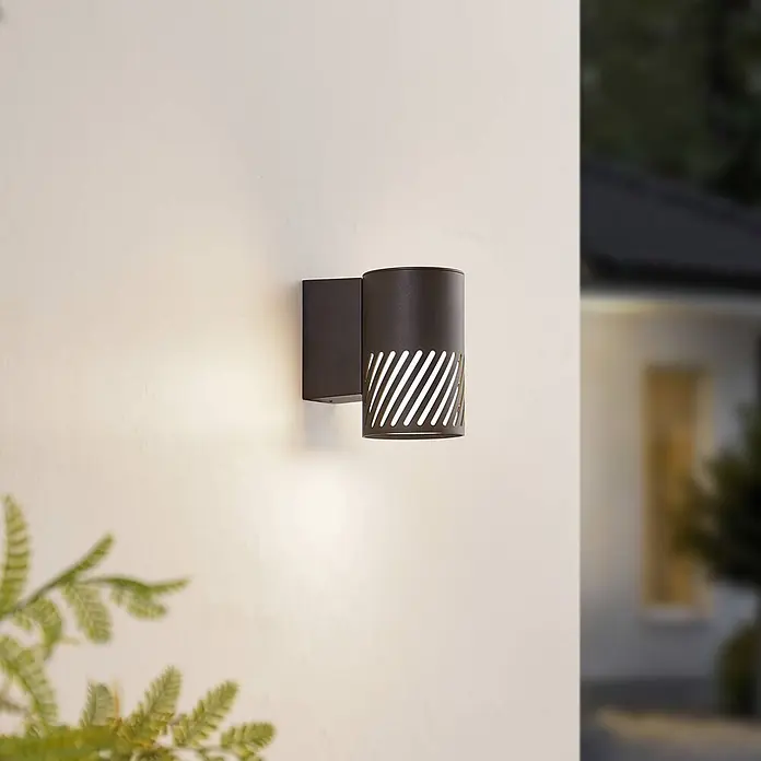 Lindby Außenwandleuchte Lurinda - 16,5 x 10,5 x 16,8 cm, schwarz, schwarz, IP44 - Schwarze zylindrische Außenwandleuchte mit diagonalen Aussparungen, an einer Wand montiert und warmes Licht spendend.