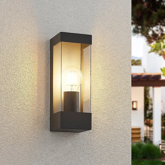 Lindby Außenwandleuchte Tilian - 8,5 x 9 x 25 cm, schwarz, schwarz, IP44 - Dunkelgraue Außenwandleuchte mit Klarglas und leuchtender Birne, an strukturierter Wand montiert, beleuchtet eine Terrasse.