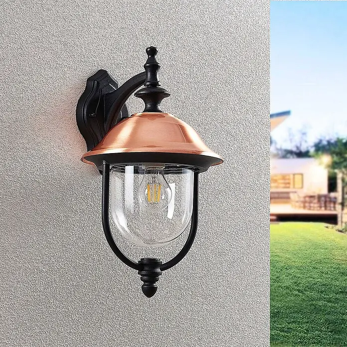 Lindby Außenwandleuchte Clint - kupfer, IP44 - Schwarze Metall-Wandleuchte mit Kupferhaube, Klarglas und LED-Glühbirne, an einer strukturierten Wand montiert.