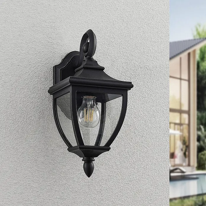 Lindby Außenwandleuchte Cerys - 19,5 x 16,5 x 37,2 cm, schwarz, IP44 - Schwarze Außenwandleuchte mit Klarglas und LED-Glühfadenlampe, montiert an einer strukturierten Wand neben einem modernen Haus.