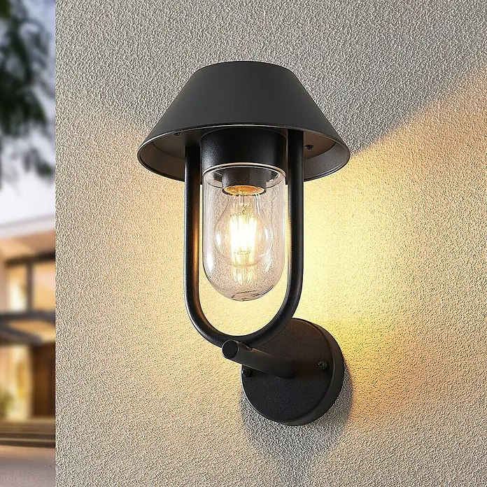 Lucande Außenwandleuchte Olinum - schwarz, schwarz, IP44 - Schwarze Outdoor-Wandleuchte mit konischem Schirm und klarem Glasdiffusor, an einer strukturierten Wand montiert und warm leuchtend.
